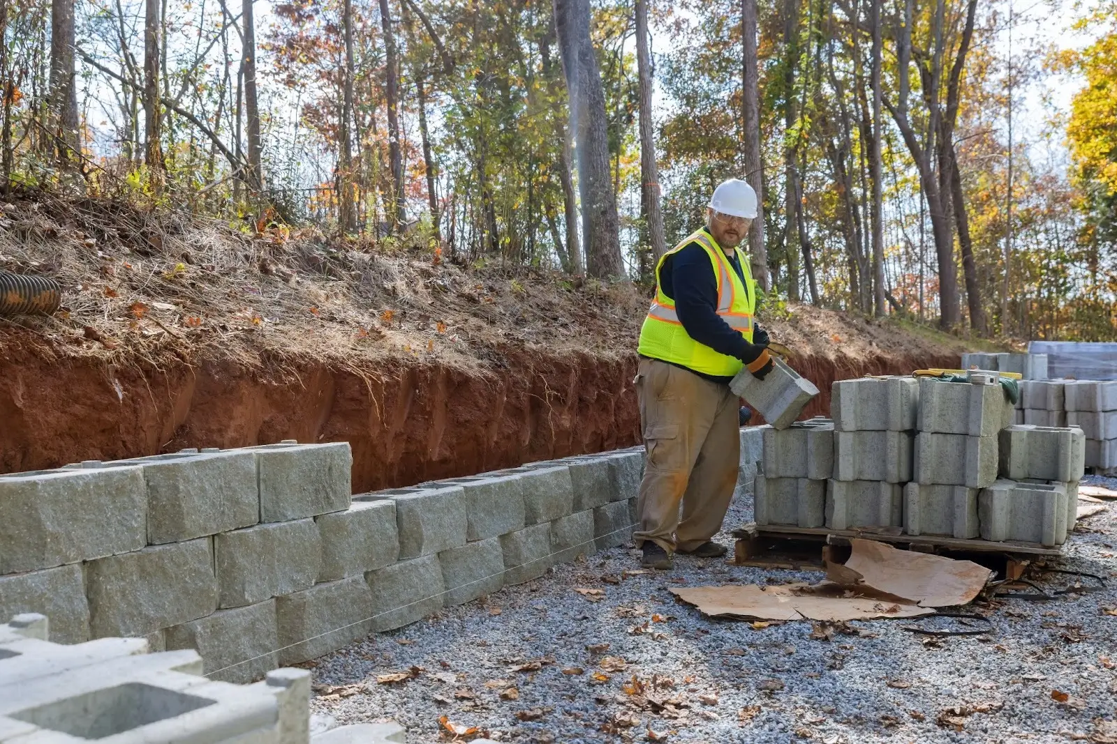 A construction worker stacks cinderblocks to form a concrete retaining wall.