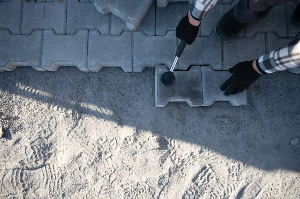 A concrete paver installation by a professional with gloves and mallet.