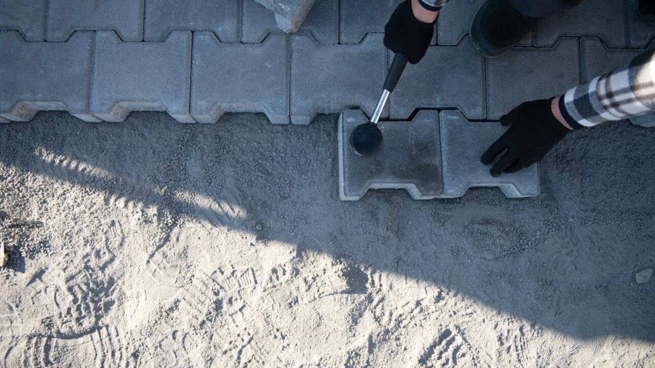 A concrete paver installation by a professional with gloves and mallet.