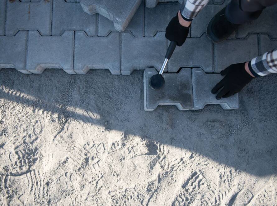 A concrete paver installation by a professional with gloves and mallet.