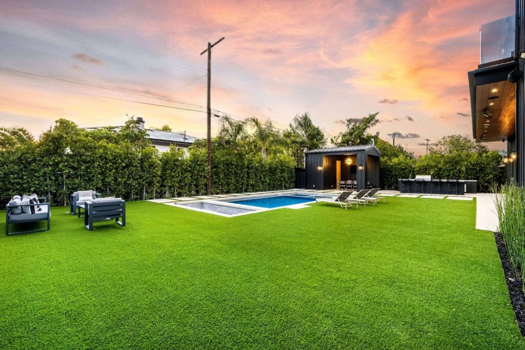 A luxurious backyard with a pool and artificial grass at sunset.