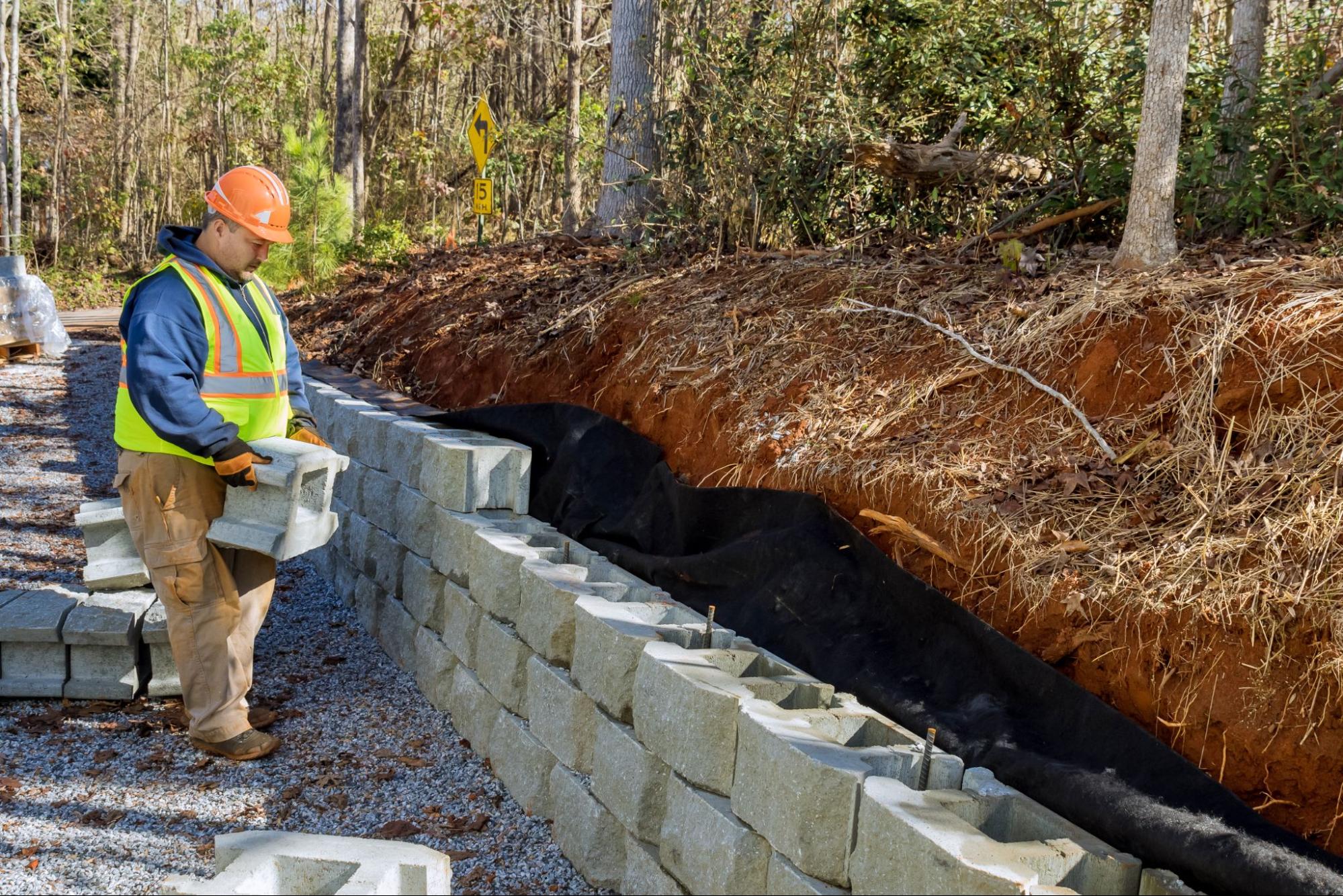 A worker builds a block wall to serve as a foundation for a retaining wall.