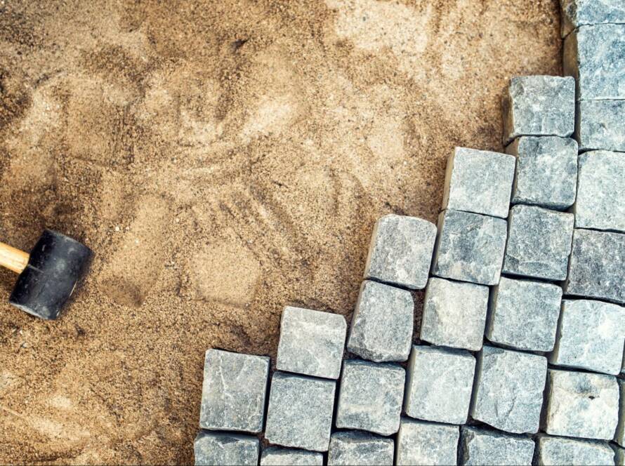 A mallet and pavers set down in a sand base prepared for paver installation.