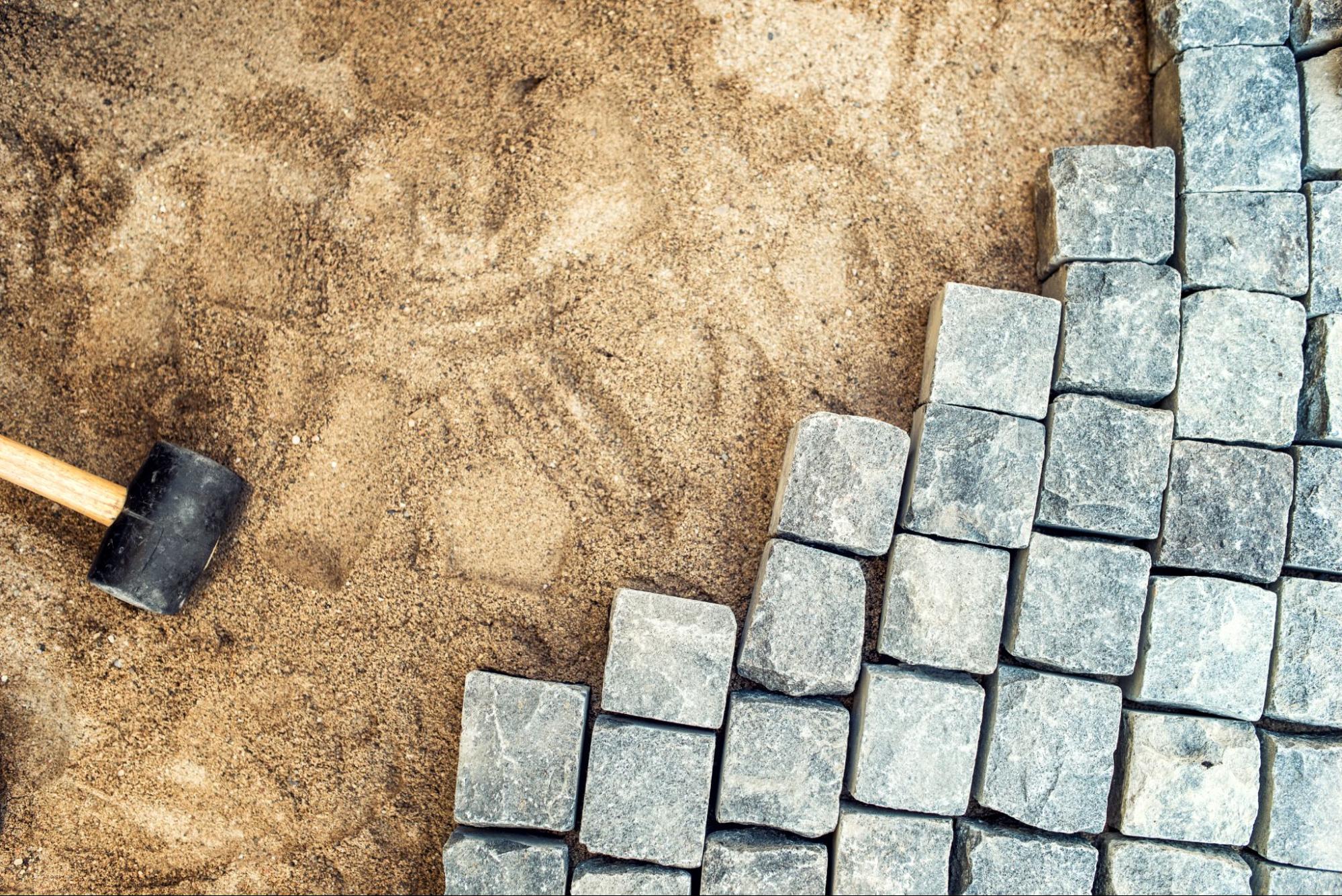 A mallet and pavers set down in a sand base prepared for paver installation.